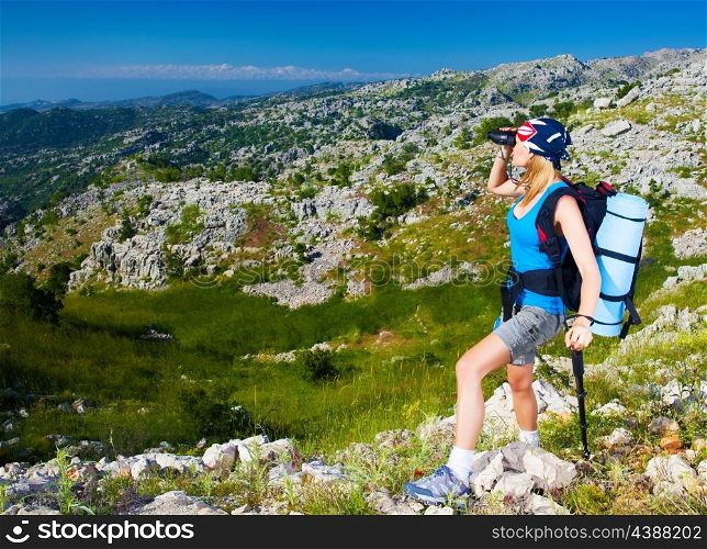 Young active female standing on the top of mountain and watching away in binocular, extreme lifestyle, traveling and trek concept