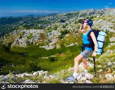 Young active female standing on the top of mountain and watching away in binocular, extreme lifestyle, traveling and trek concept