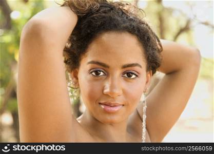 Young-adult African American woman with arms behind head holding hair up.