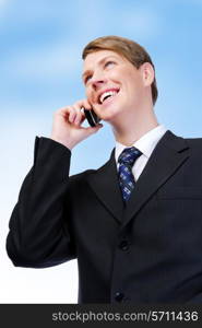 Young adult american businessman talking on mobile phone. On the blue sky background