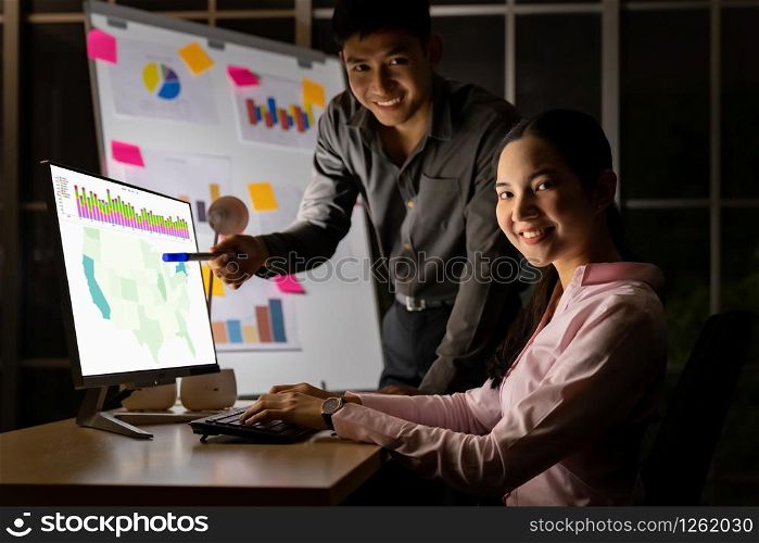 Young adult asian businessman and businesswoman work with analysis graph on white board late at night in their office with desktop computer. Using as hard working and working late concept.