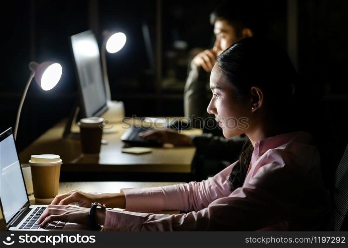Young adult asian businessman and woman working late at night in their office with desktop computer and laptop. Using as hard working and working late concept.