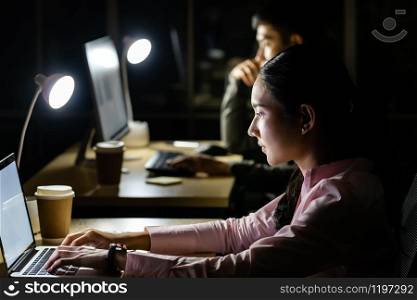 Young adult asian businessman and woman working late at night in their office with desktop computer and laptop. Using as hard working and working late concept.