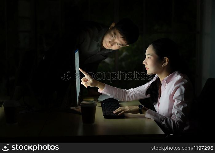 Young adult asian businessman dicuss with collegue about work late at night in their office with desktop computer. Using as hard working and working late concept.