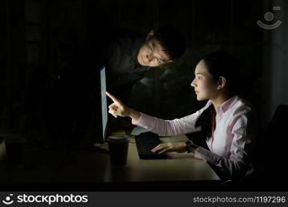 Young adult asian businessman dicuss with collegue about work late at night in their office with desktop computer. Using as hard working and working late concept.