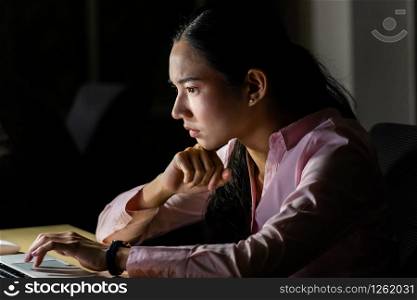 Young adult asian businesswoman working hard and late at night in her office with laptop computer. Using as hard working and working late concept.