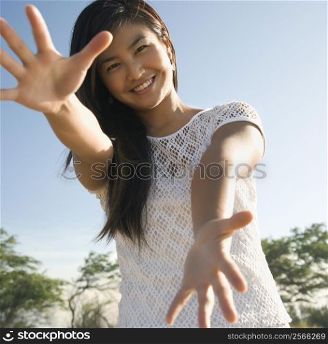 Young adult Asian female with arms and hands stretched out toward viewer.