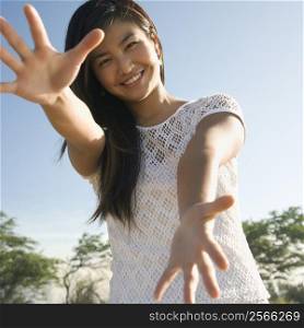 Young adult Asian female with arms and hands stretched out toward viewer.