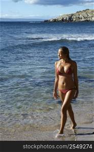 Young adult Asian Filipino female in bikini walking on beach in Maui Hawaii.