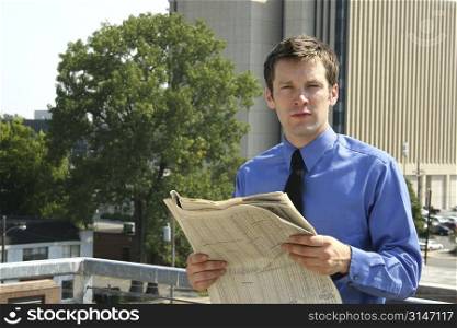 Young adult business man reading a newspaper with big city buildings in background.