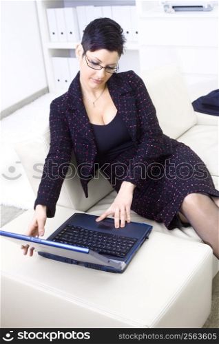 Young adult businesswoman sitting on sofa at office and working on laptop computer.
