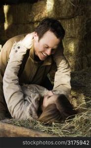 Young adult Caucasian couple laying in hay embracing.