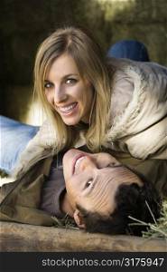 Young adult Caucasian couple lying in hay and smiling up at viewer.