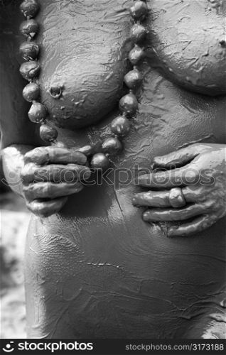 Young adult Caucasian female nude covered in mud holding necklace.