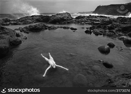 Young adult Caucasian female nude floating in water in rocky Maui, Hawaii coast.