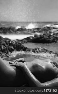 Young adult Caucasian female nude lying on rocky coast of Maui, Hawaii.