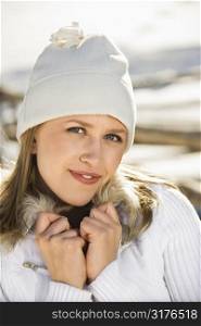 Young adult Caucasian female outdoors in winter wearing knit cap and coat and smiling at viewer.