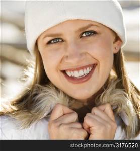 Young adult Caucasian female wearing knit cap holding fur collar and smiling at viewer.
