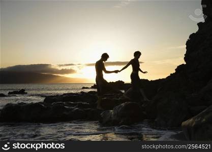 Young adult Caucasian male and female silhouetted on beach.