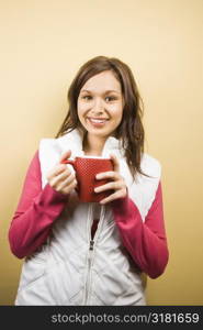 Young adult Caucasian woman holding coffee cup and smiling at viewer.