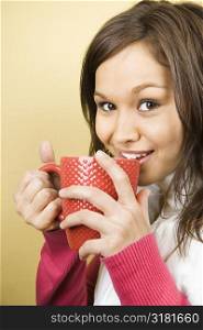 Young adult Caucasian woman holding coffee cup to lips and smiling at viewer.