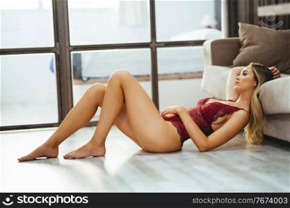 Young adult caucasian woman in red lingerie lying on the floor. Caucasian girl in red lingerie lying on the floor