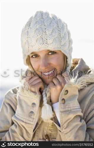 Young adult Caucasian woman in winter attire holding collar and smiling at viewer.