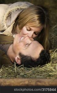 Young adult Caucasian woman kissing boyfriend while lying in hay.