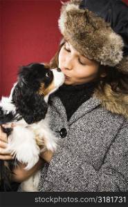 Young adult Caucasian woman wearing fur hat kissing King Charles Spaniel.
