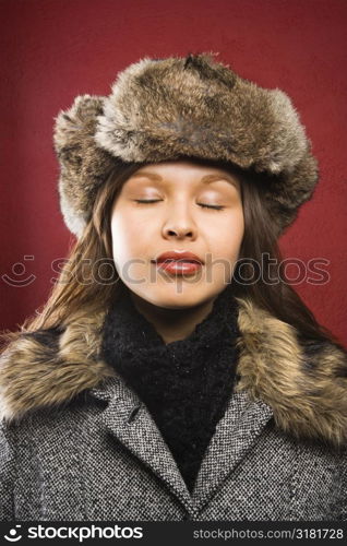 Young adult Caucasian woman wearing fur hat with eyes closed.