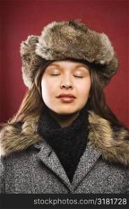 Young adult Caucasian woman wearing fur hat with eyes closed.