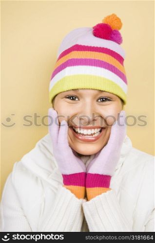 Young adult Caucasian woman wearing winter hat and gloves with hands to face smiling at viewer.