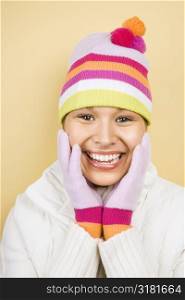 Young adult Caucasian woman wearing winter hat and gloves with hands to face smiling at viewer.