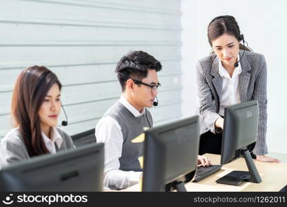 Young adult confidence with smiling female supervisor standing in front of working table of operator team ain a call centre to monitor her employee. Using for woman leadership concept