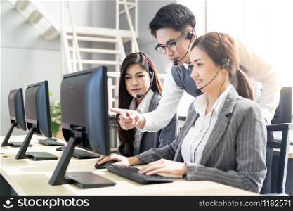 Young adult confidence with smiling supervisor teaching to his team of operator team agent with headsets and desktop computer in a call center to monitor her employee.