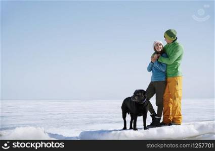 Young adult couple outdoors with dog having fun in winter landscape