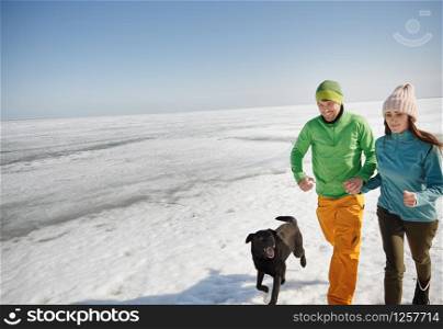 Young adult couple outdoors with dog having fun in winter landscape