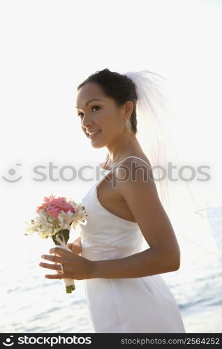 Young adult female Caucasian bride holding bouquet on beach.