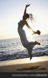 Young adult female Caucasian bride jumping on beach.