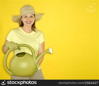 Young adult female Caucasian holding watering can wearing straw hat.