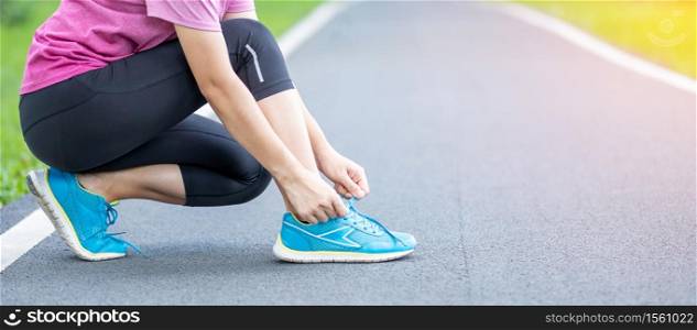 Young adult female in sportswear tying shoelace in the park outdoor, athlete runner woman ready for running and jogging in morning. Exercise, wellness, healthy lifestyle and workout concept