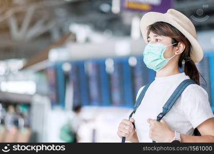 Young adult female wearing surgical mask in airport terminal, protection Coronavirus disease (Covid-19) infection, Asian woman traveler with hat ready to travel. New Normal and travel bubble concept