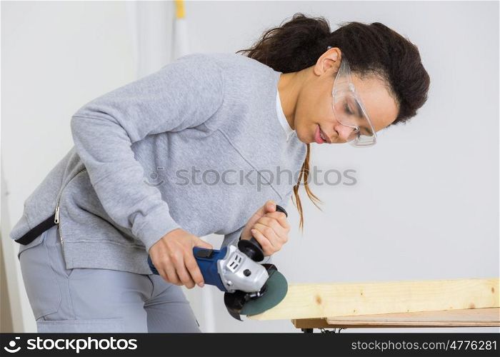young adult female worker grinding plank with electric grinder