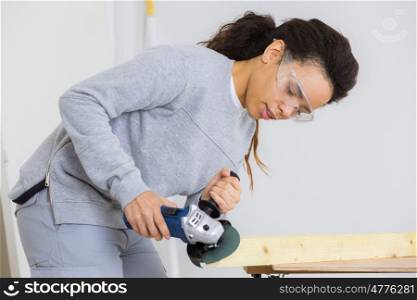young adult female worker grinding plank with electric grinder