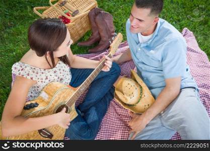 Young Adult Girl Playing Guitar with Boyfriend In The Park.