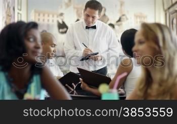 Young adult hispanic couple dining out in restaurant and talking to waiter in bow tie. Dolly shot
