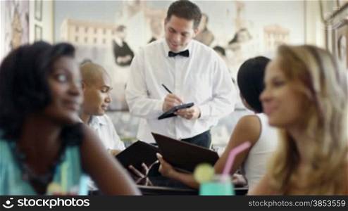 Young adult hispanic couple dining out in restaurant and talking to waiter in bow tie. Dolly shot