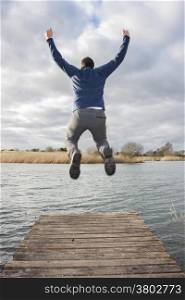 Young adult jumping on the edge of a dock