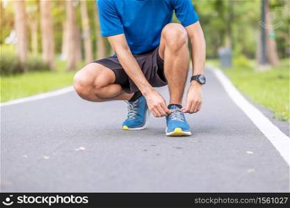 Young adult male in sportswear tying shoelace in the park outdoor, athlete runner man ready for running and jogging in morning. Exercise, wellness, healthy lifestyle and workout concept