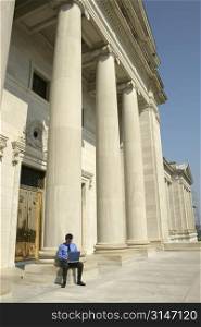 Young adult male working on a laptop computer in front of a government building.